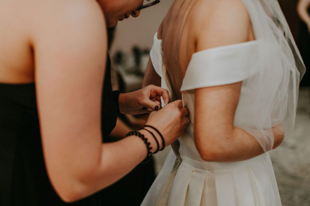 bridesmaid buttoning a bride's wedding dress