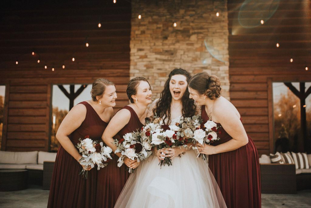 bride and bridesmaids laughing together in front of The Heartland Lodge, a wedding venue in Kansas City, Missouri
